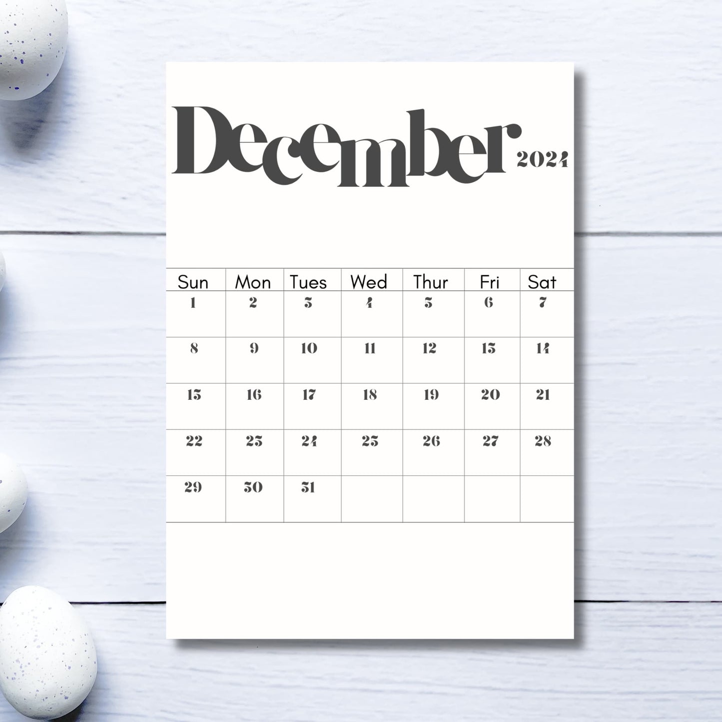 2024 December printed sheet on light grey wooden table with white pebbles