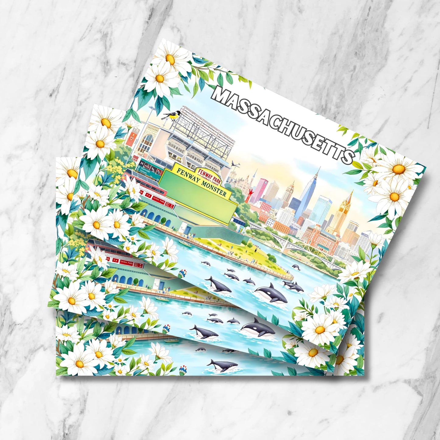 Stack of Massachusetts prints with Fenway Park, Boston skyline, whales, chickadee and daisy flowers on marble background.