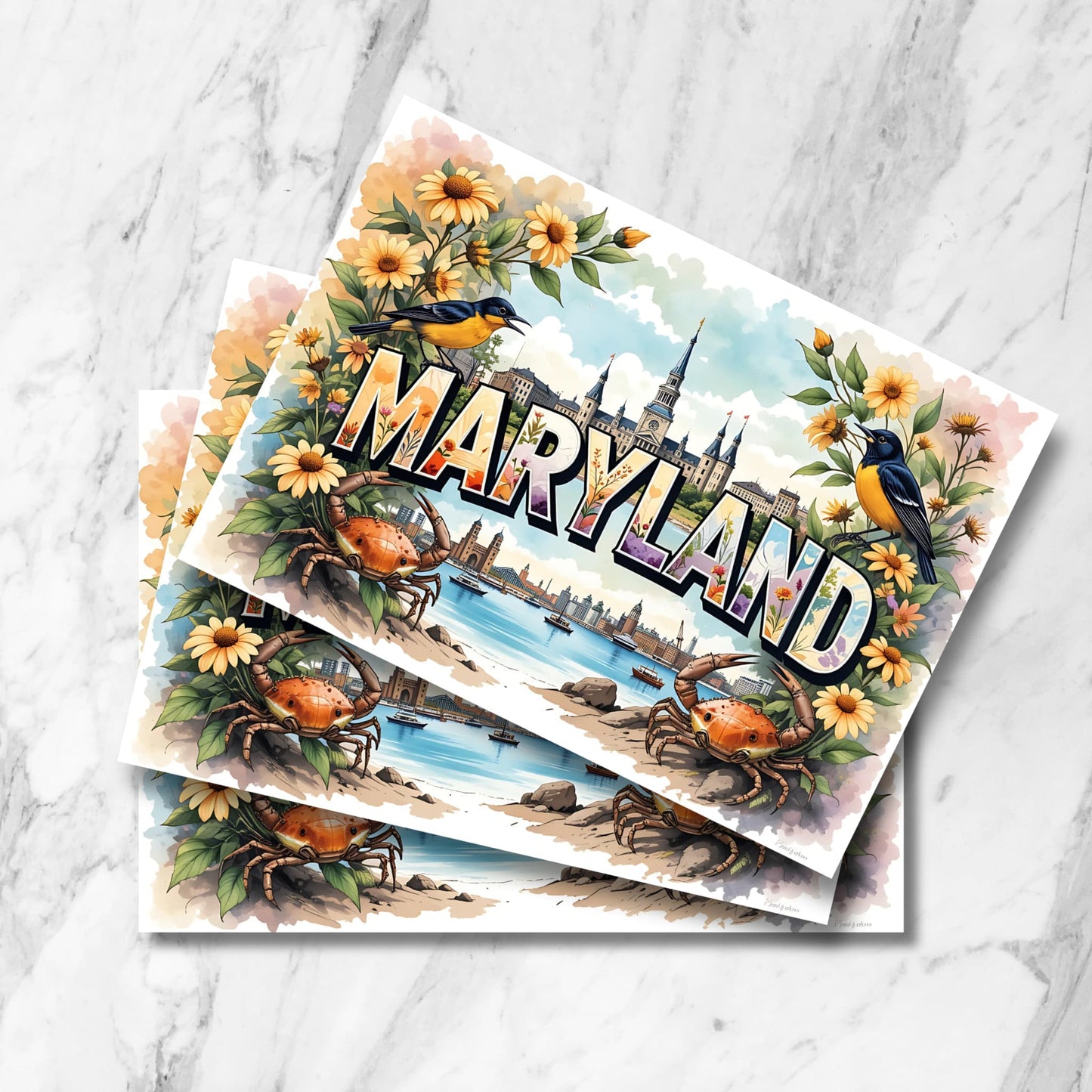 Stack of Maryland watercolor prints featuring Annapolis harbor, blue crabs, Baltimore orioles and black-eyed susan flowers on marble background.