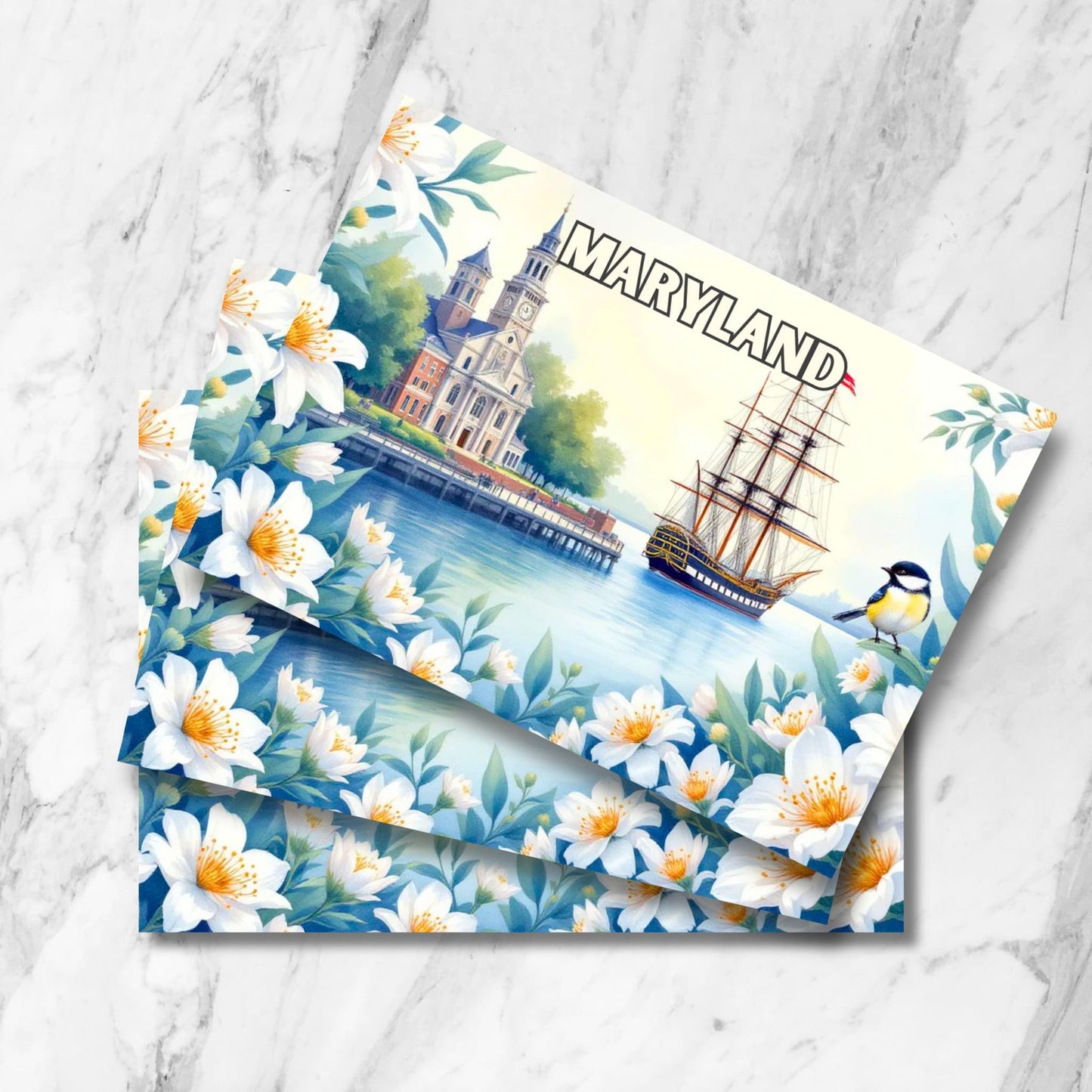 Stack of Maryland waterfront prints featuring historic church, tall ship, chickadee bird and white dogwood flowers on marble background.
