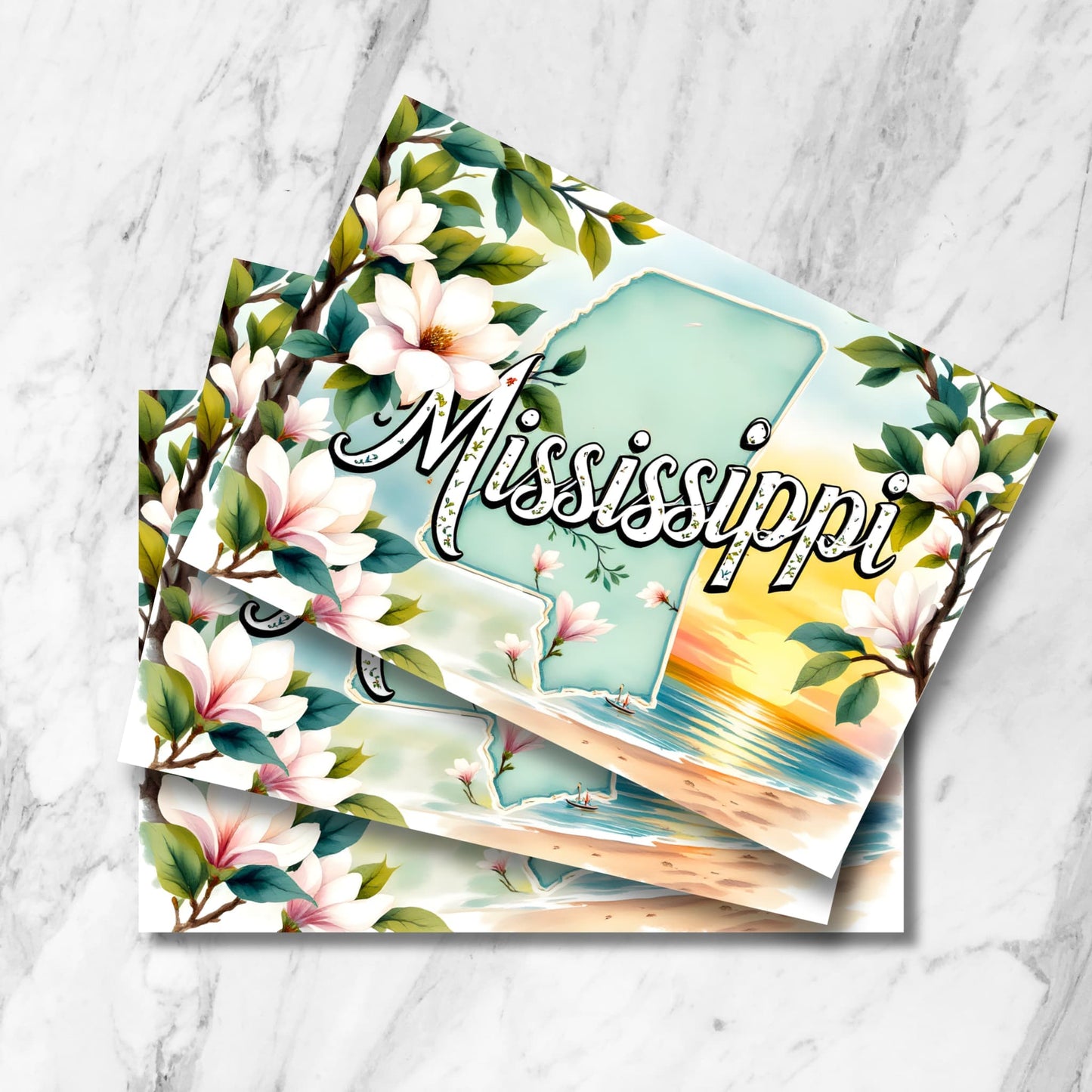 Stack of Mississippi postcards featuring state outline, magnolia blossoms and Gulf Coast sunset beach scene on marble background.