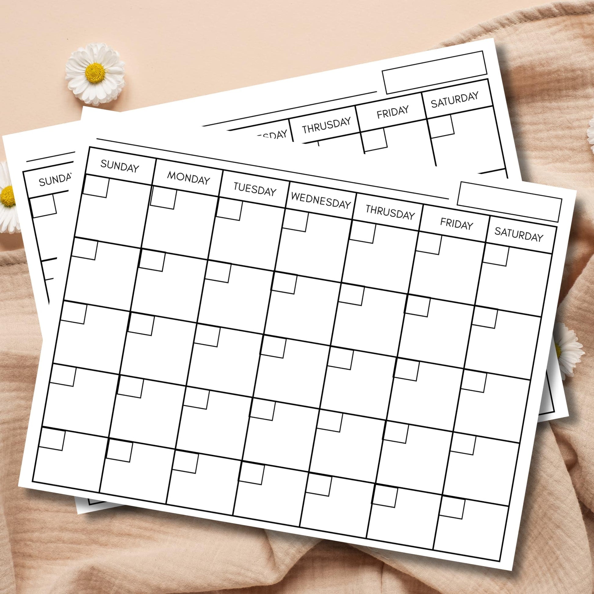 Reusable perpetual calendar templates with date boxes stacked on linen fabric with white daisies.