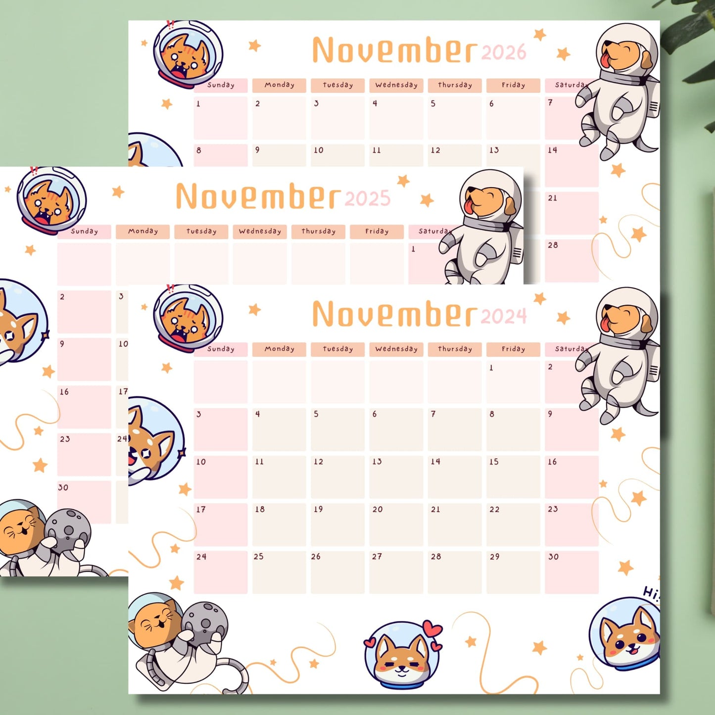 Stacked monthly calendars for November 2024-2026 with playful astronaut puppies and moon-themed illustrations, displayed on sage green background with plant decor.