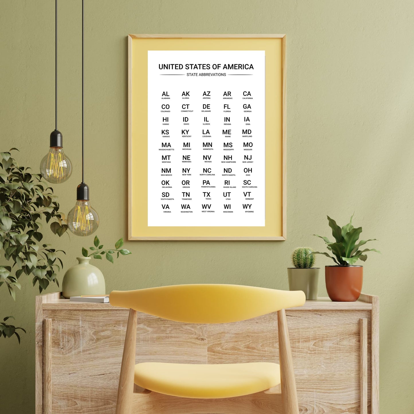 Framed US state abbreviations chart displayed in a yellow frame above a desk with indoor plants, ideal for classroom or home study space