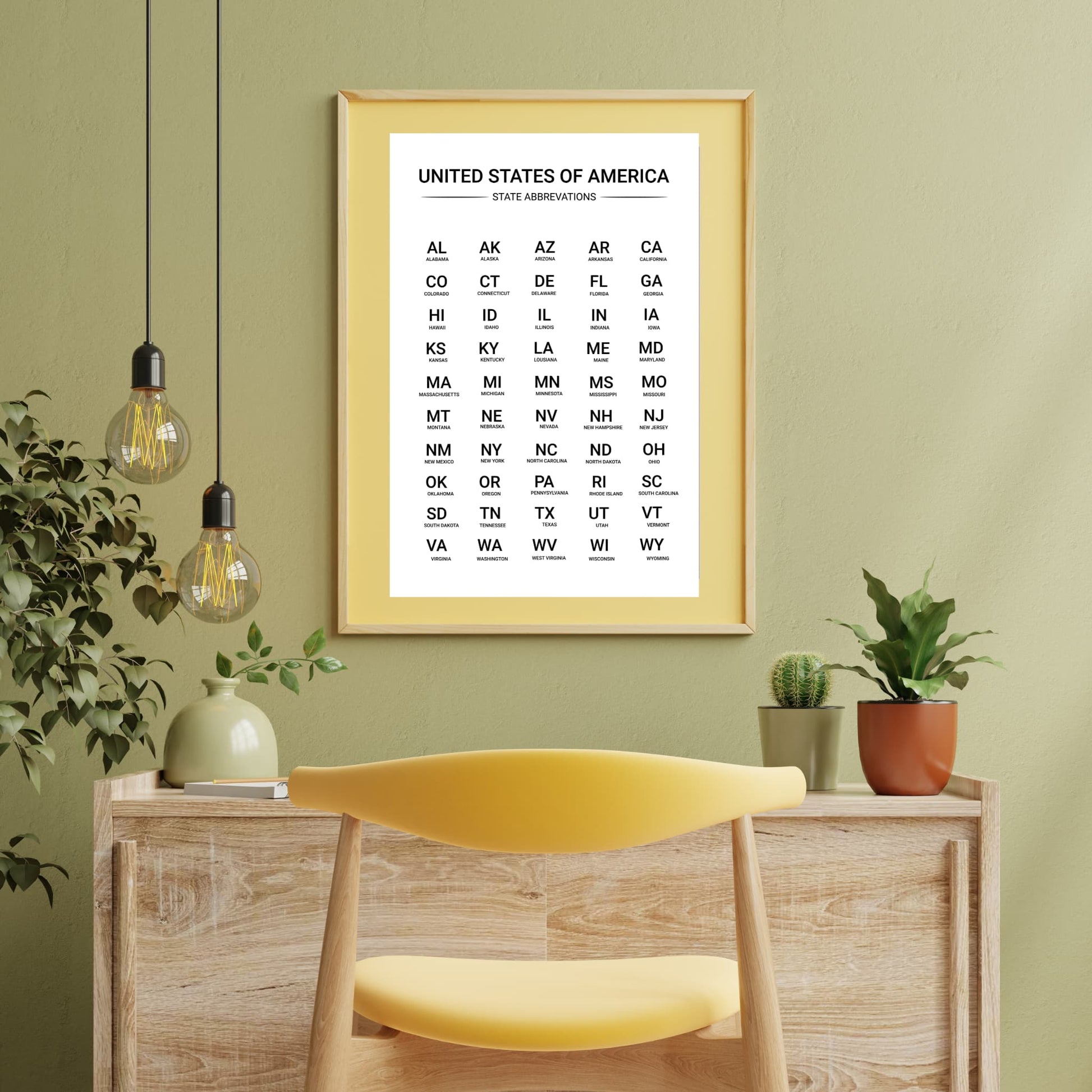 Framed US state abbreviations chart displayed in a yellow frame above a desk with indoor plants, ideal for classroom or home study space