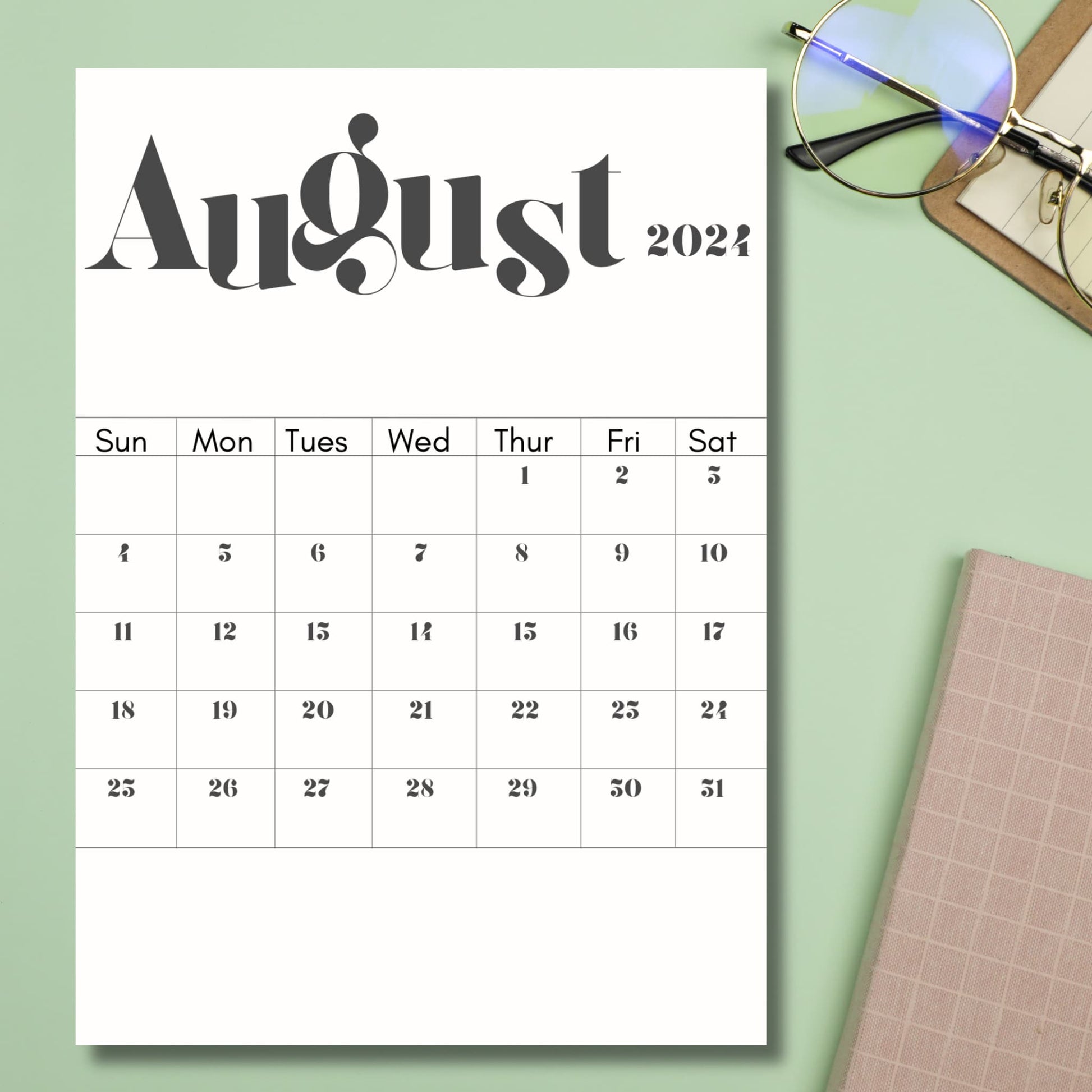2024 August printed calendar sheet lying on top of green table with notebook and glasses besides it.