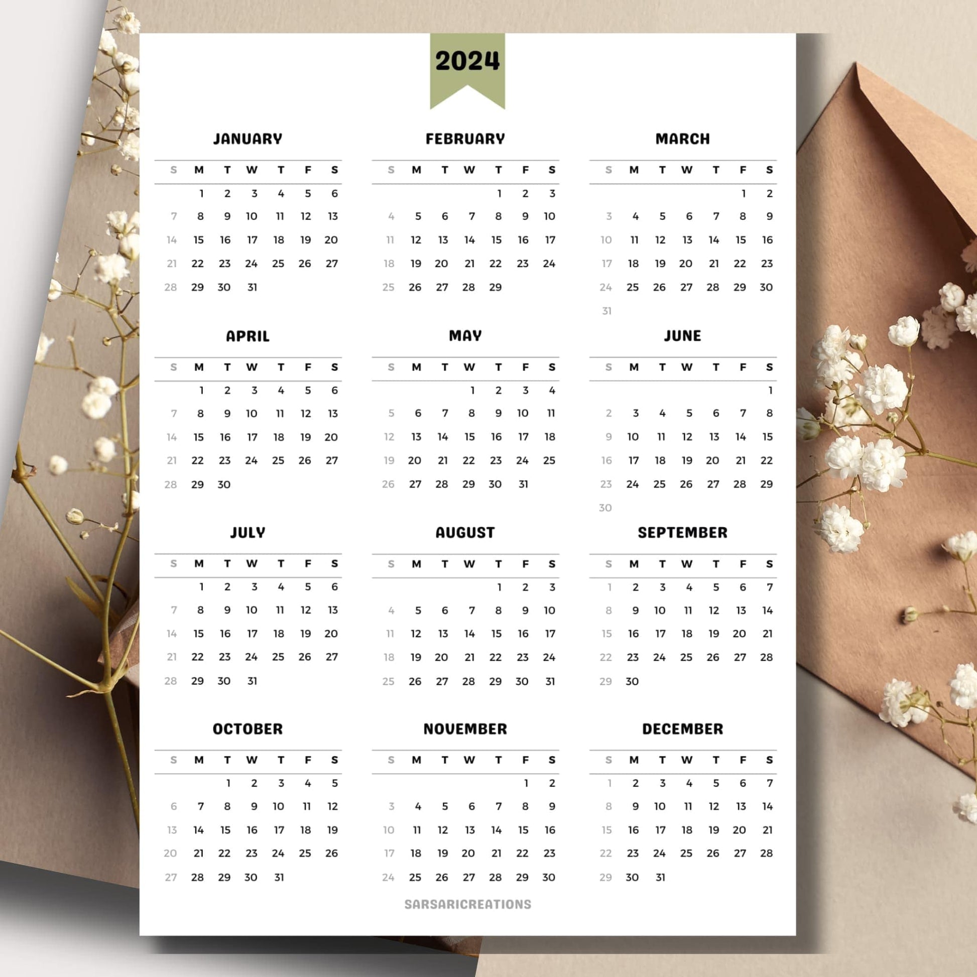 Minimalist 2024 full year calendar page on a table with envelope and small white flowers in the background.