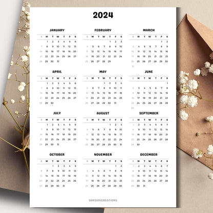Printed page of the 2024 full year calendar on a table with an envelope and small white flowers in the background.