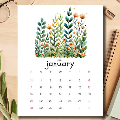 Evergreen Embrace January 2024 calendar displayed on a light brown wooden desk with school supplies like notebooks, pencils, and sharpeners.