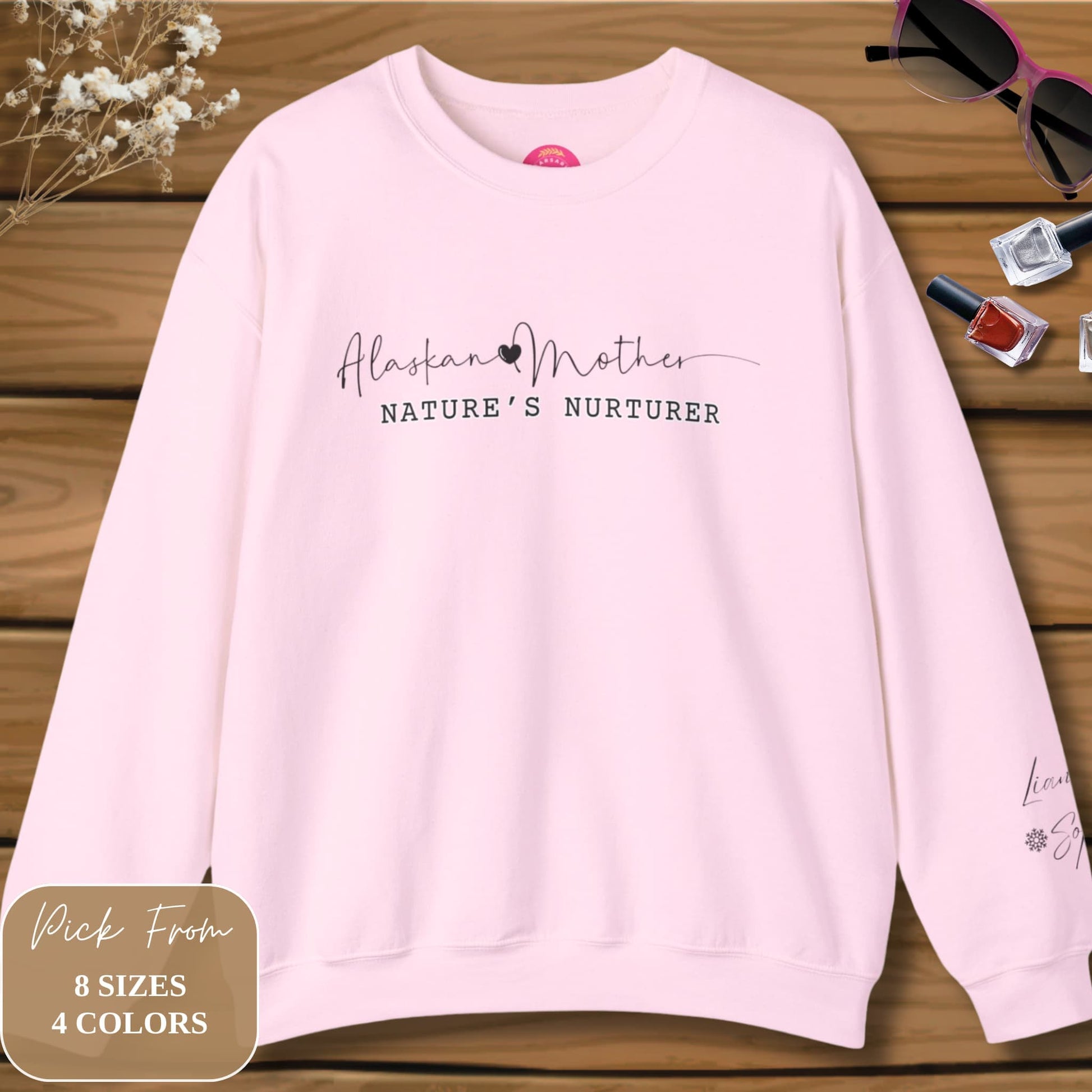 Alaskan Mother Personalized Crewneck Sweatshirt displayed on a wooden surface, adorned with flowers and women's accessories in an elegant flatlay.