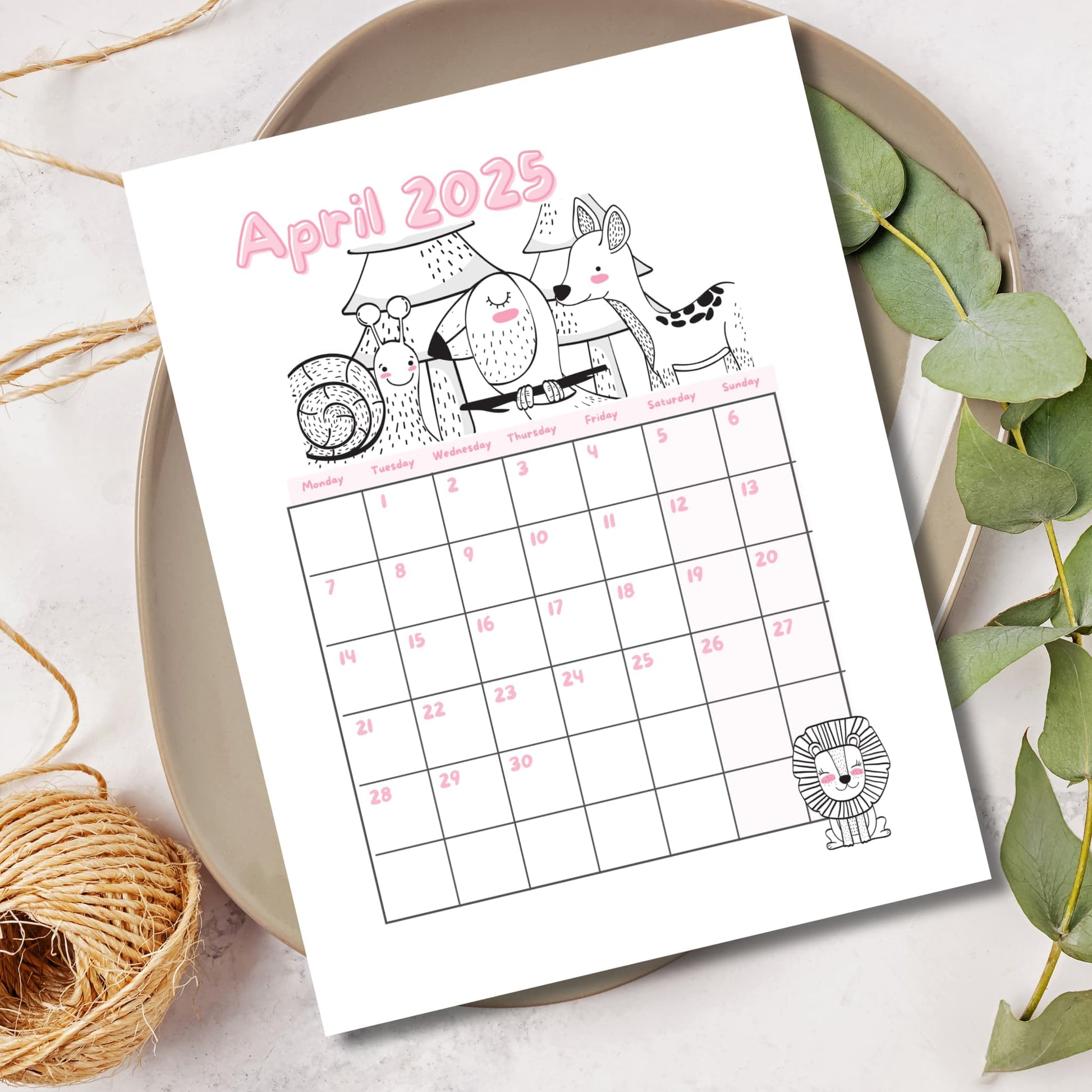 April 2025 calendar with woodland creatures line art. Pink lettering with Monday-start grid displayed on ceramic plate with eucalyptus and natural rope elements.