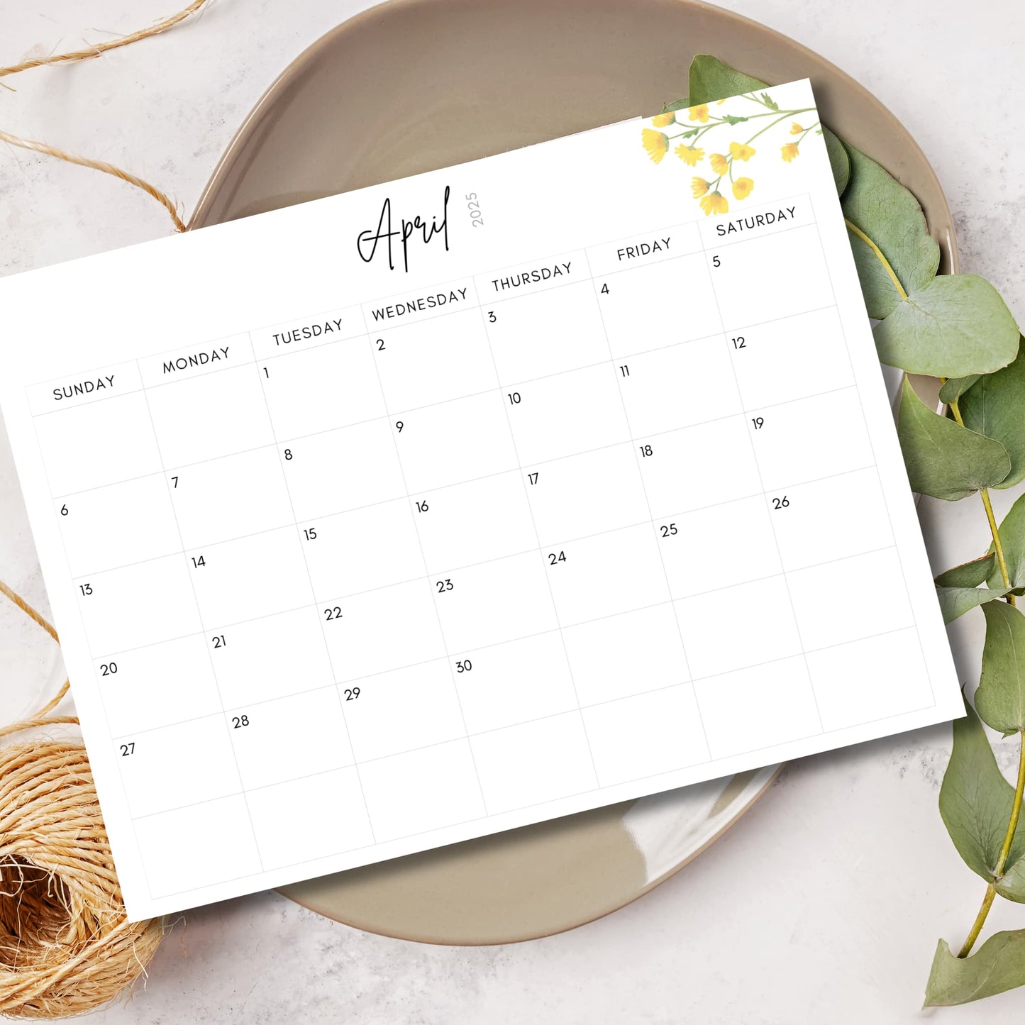 April 2025 calendar page with simple clean design, script handwriting, yellow floral accent in corner, styled with eucalyptus leaves and natural decor