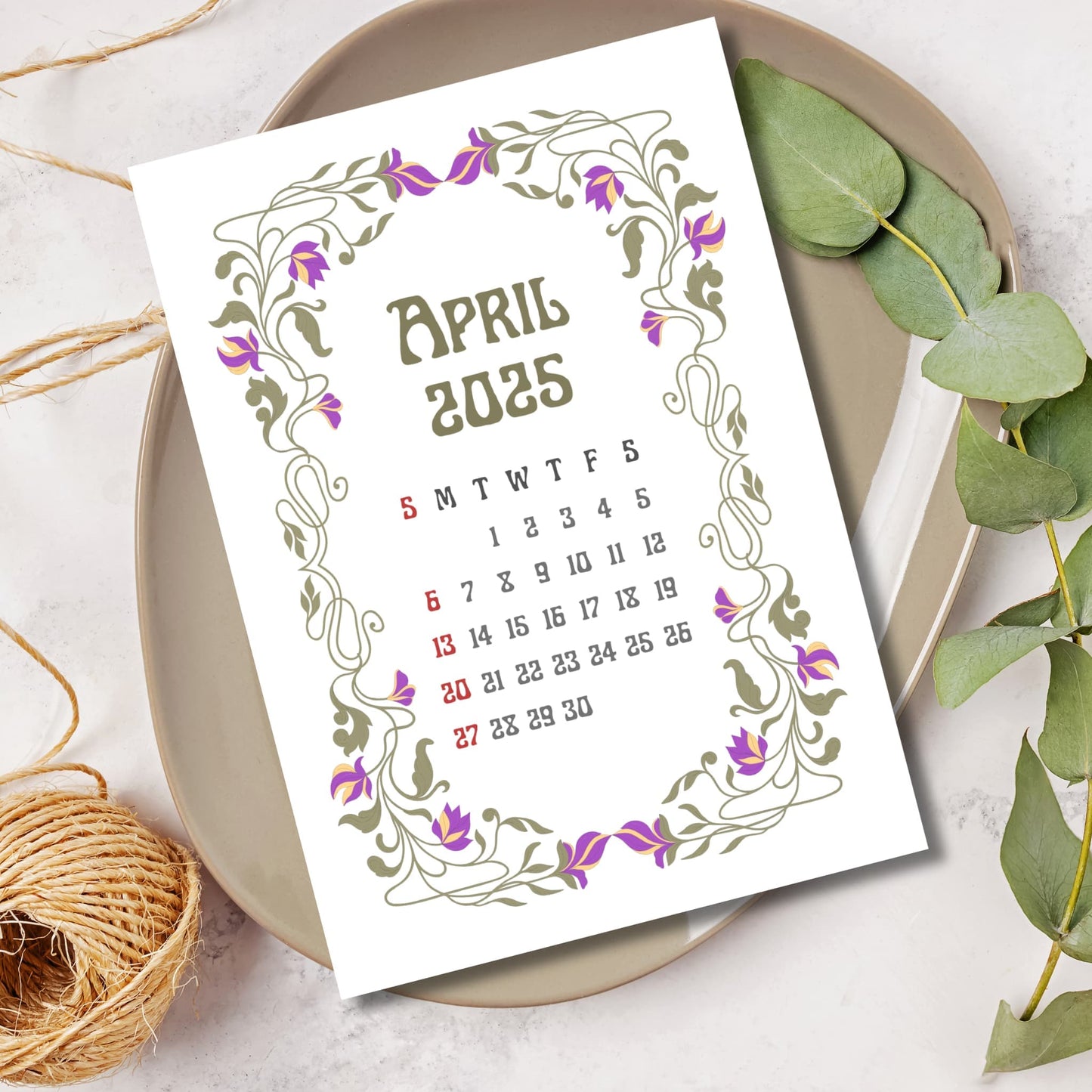 April 2025 calendar page featuring Art Nouveau frame with purple tulip motifs, styled with eucalyptus leaves and natural twine on ceramic plate