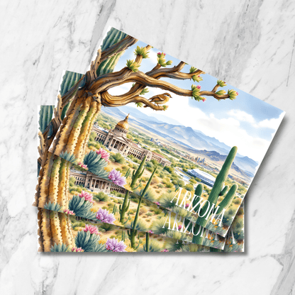 Stacked prints of vintage-style Arizona State Capitol illustration with flowering saguaro cactus, desert wildflowers, mountain ranges, and Phoenix skyline, displayed on marble surface with desert bird detail