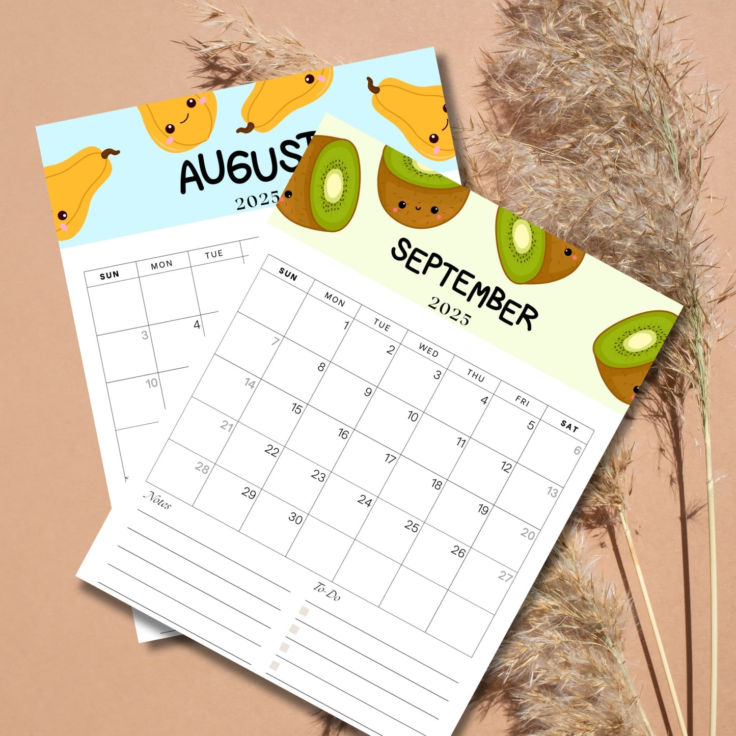 August 2025 calendar page with cute banana illustrations and September 2025 calendar page with kiwi fruit characters, displayed on beige background with dried pampas grass. Both pages include notes and to-do sections.