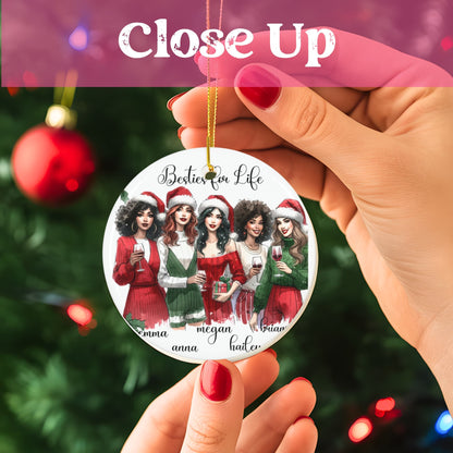 Close-up view of Besties for Life Christmas ornament held against decorated tree, showing detailed watercolor illustration of five friends in red and green holiday attire with personalized names