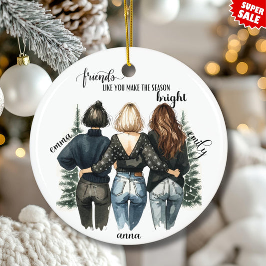 Personalized best friends ceramic ornament displayed on Christmas tree with cozy white knit blanket, frosted pine branches, and festive bokeh lights, featuring three friends illustration with 'Make the Season Bright' sentiment and customizable names