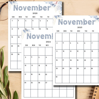 Stacked monthly calendars November 2024-2026 with delicate blue-gray floral design, displayed on wooden surface with green plant decor