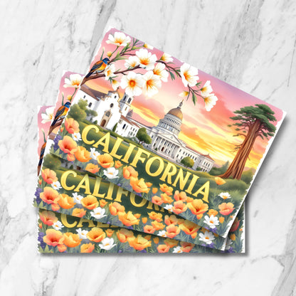 Vintage-style California postcards showing State Capitol, Spanish Mission, and giant sequoia tree framed by orange poppies and cherry blossoms with sunset sky, displayed as stacked prints on marble background