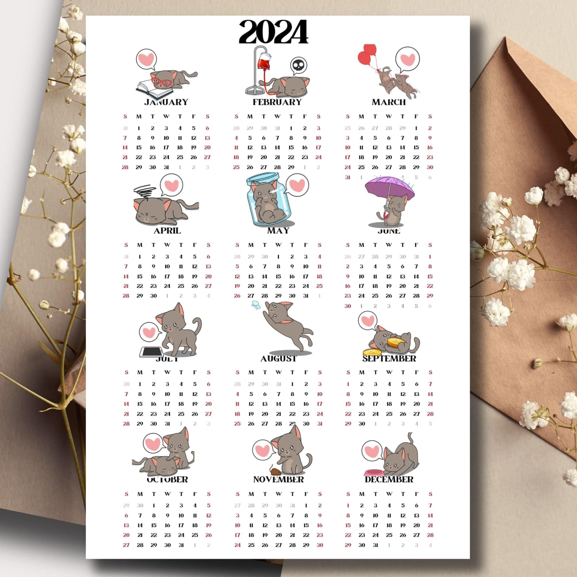 Cute cat illustrated 2024 full year calendar on a table with an envelope and small white flowers in the background.