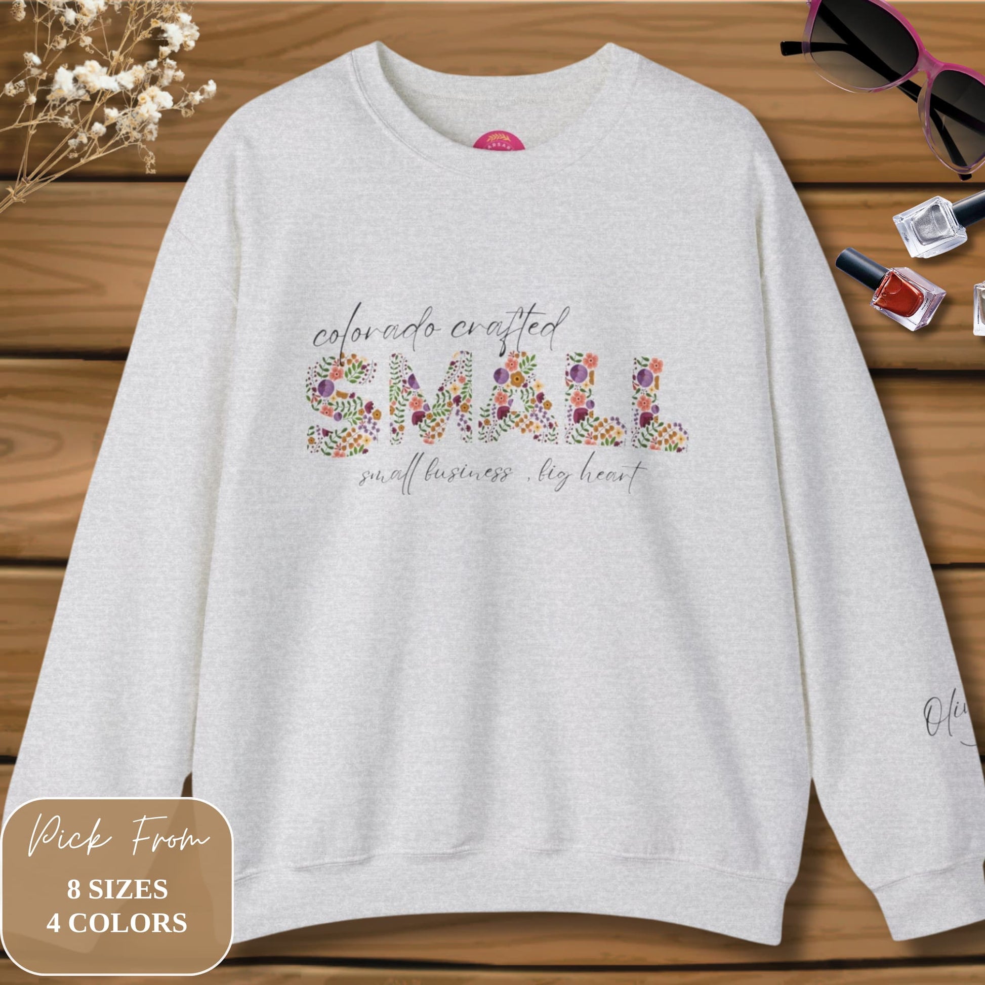 Custom Colorado Crewneck Sweatshirt in Pink Laid on Wooden Background with Stylish Women's Accessories.