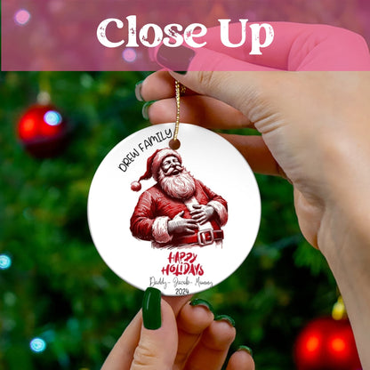 Close-up view of personalized ceramic ornament with laughing Santa design and family names against Christmas tree backdrop