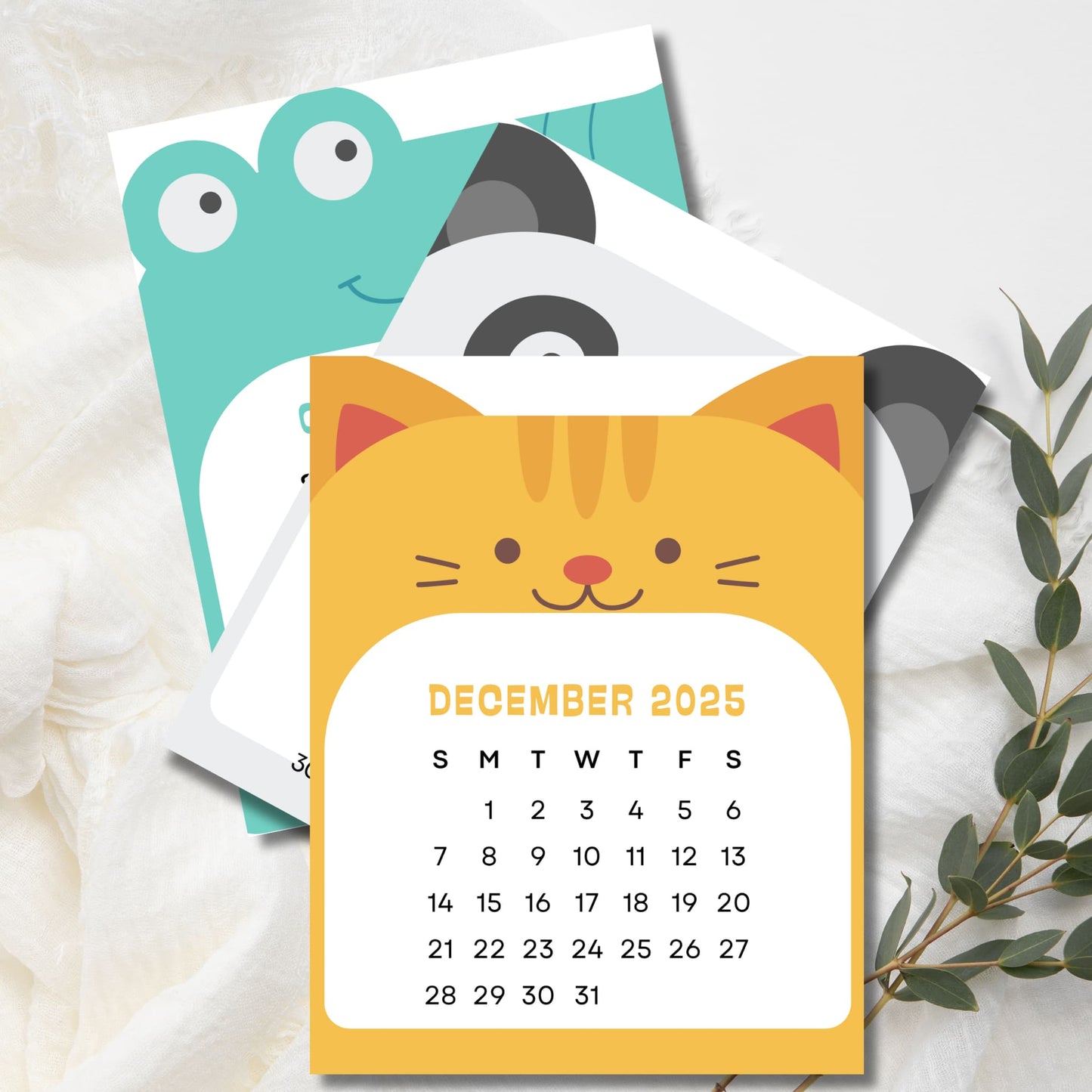 December 2025 calendar with yellow cat design, featuring frog and panda pages behind. Sunday-start grid layout with eucalyptus sprig decoration.