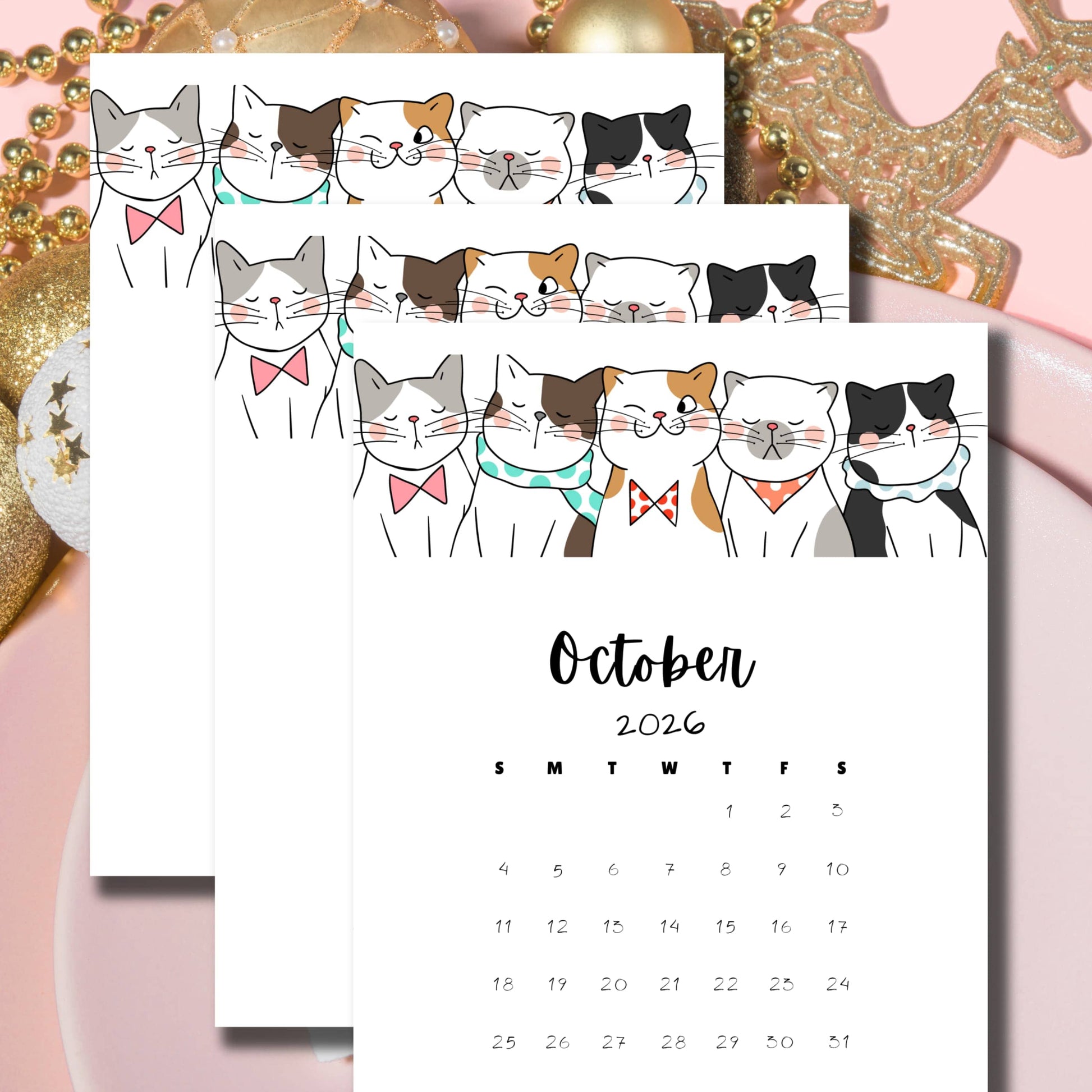 Flatlay of October 2024-2026 calendars featuring whimsical cat designs, arranged on pink background with golden holiday decorations, showcasing the multi-year planning option.