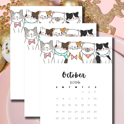 Flatlay of October 2024-2026 calendars featuring whimsical cat designs, arranged on pink background with golden holiday decorations, showcasing the multi-year planning option.