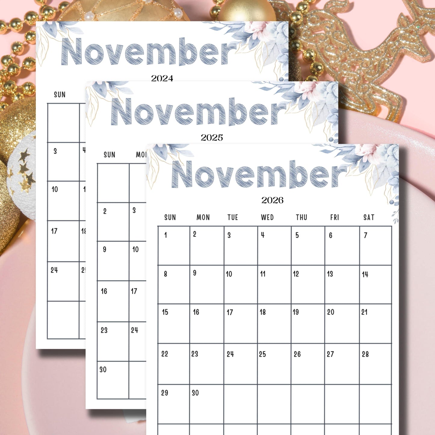 Layered November calendars 2024-2026 featuring blue floral watercolor accents, displayed with golden reindeer ornaments and beads on pink background