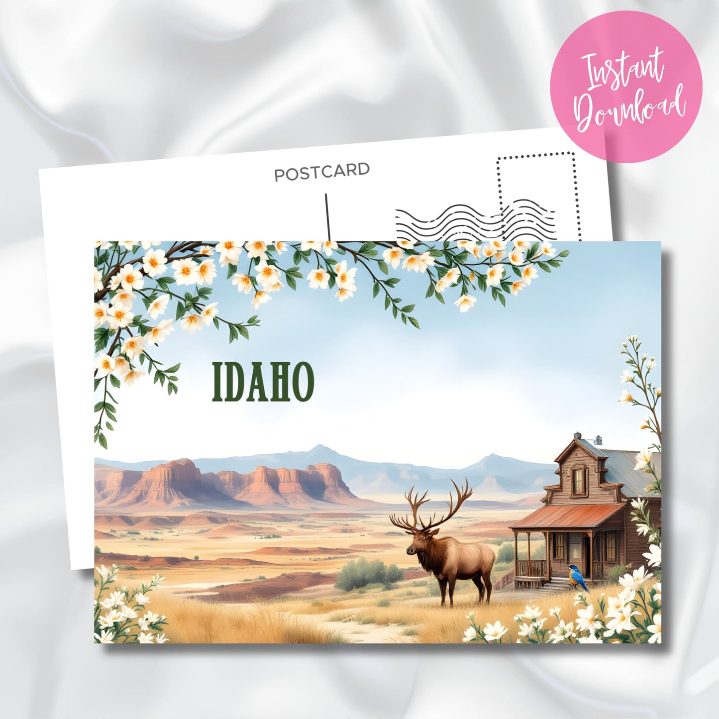 Digital download preview of Idaho souvenir postcard with desert mountains, wild elk, rustic cabin, bluebird, and flowering branches against soft blue sky backdrop