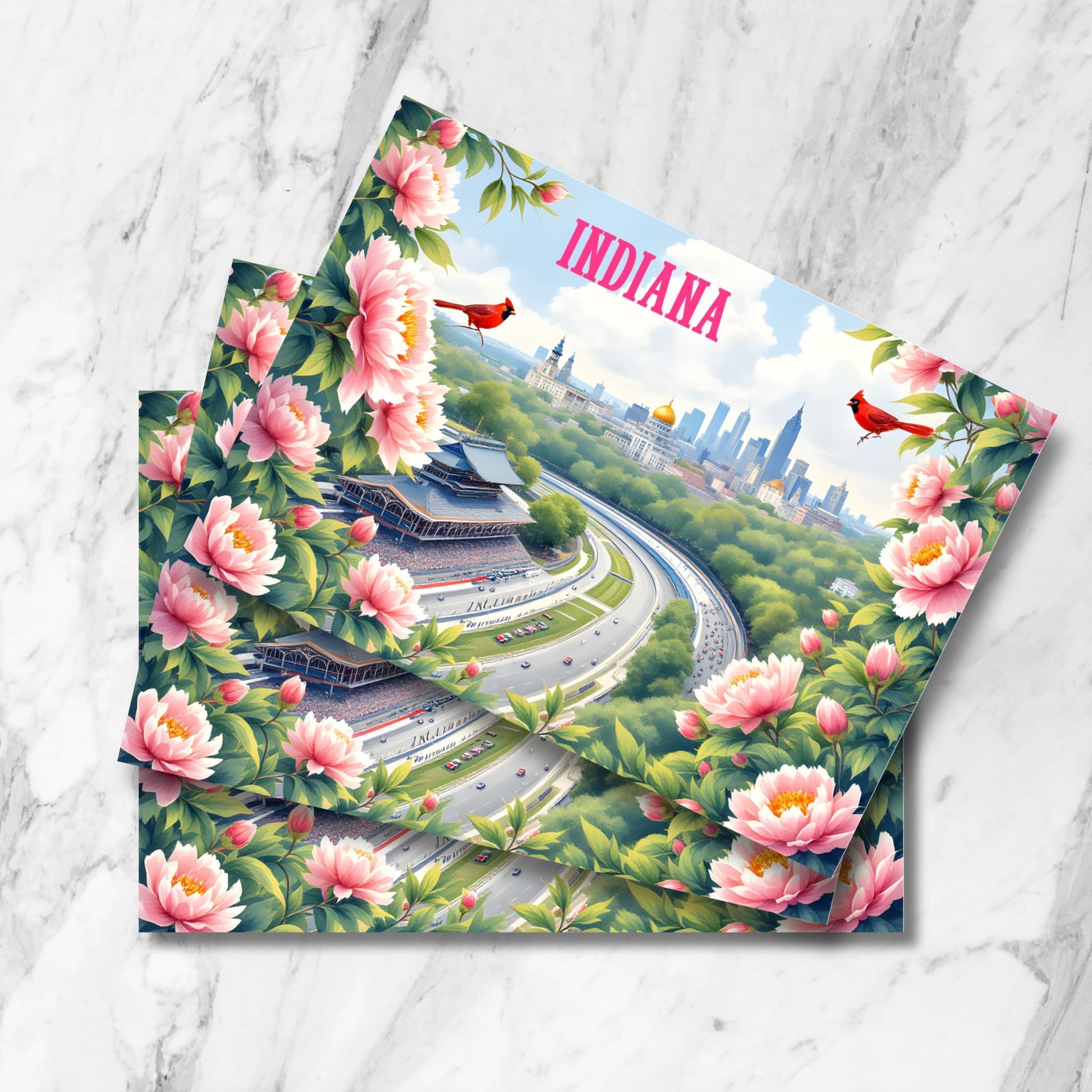 Artistic Indiana travel postcard featuring Indianapolis Motor Speedway surrounded by pink peonies, with skyline backdrop, red cardinals, and golden dome statehouse. Multiple cards shown stacked on marble surface.