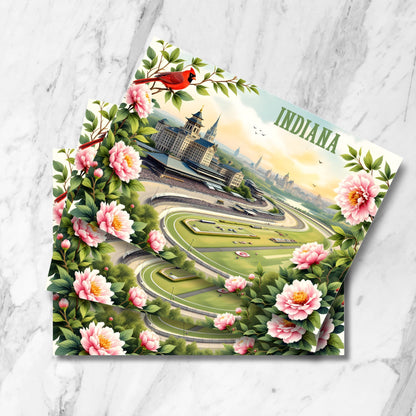 Vintage-style aerial view of Indianapolis Motor Speedway at sunset with pink peonies and red cardinal border. Features historic pagoda building, grandstands, and detailed racing track with city skyline in background.