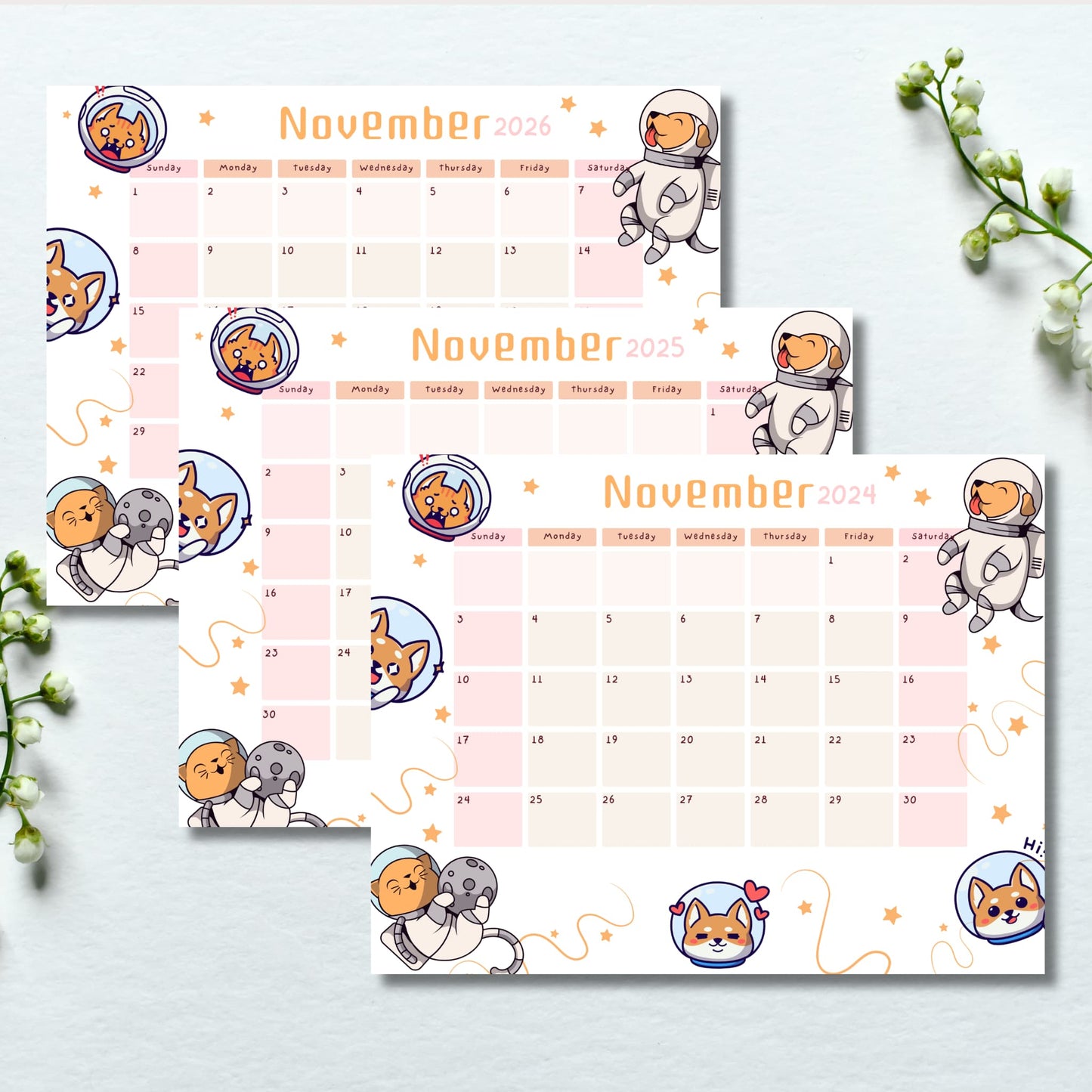 Flat lay of November calendars 2024-2026 featuring adorable space puppies and moon illustrations, styled with white lily of the valley flowers on light background.