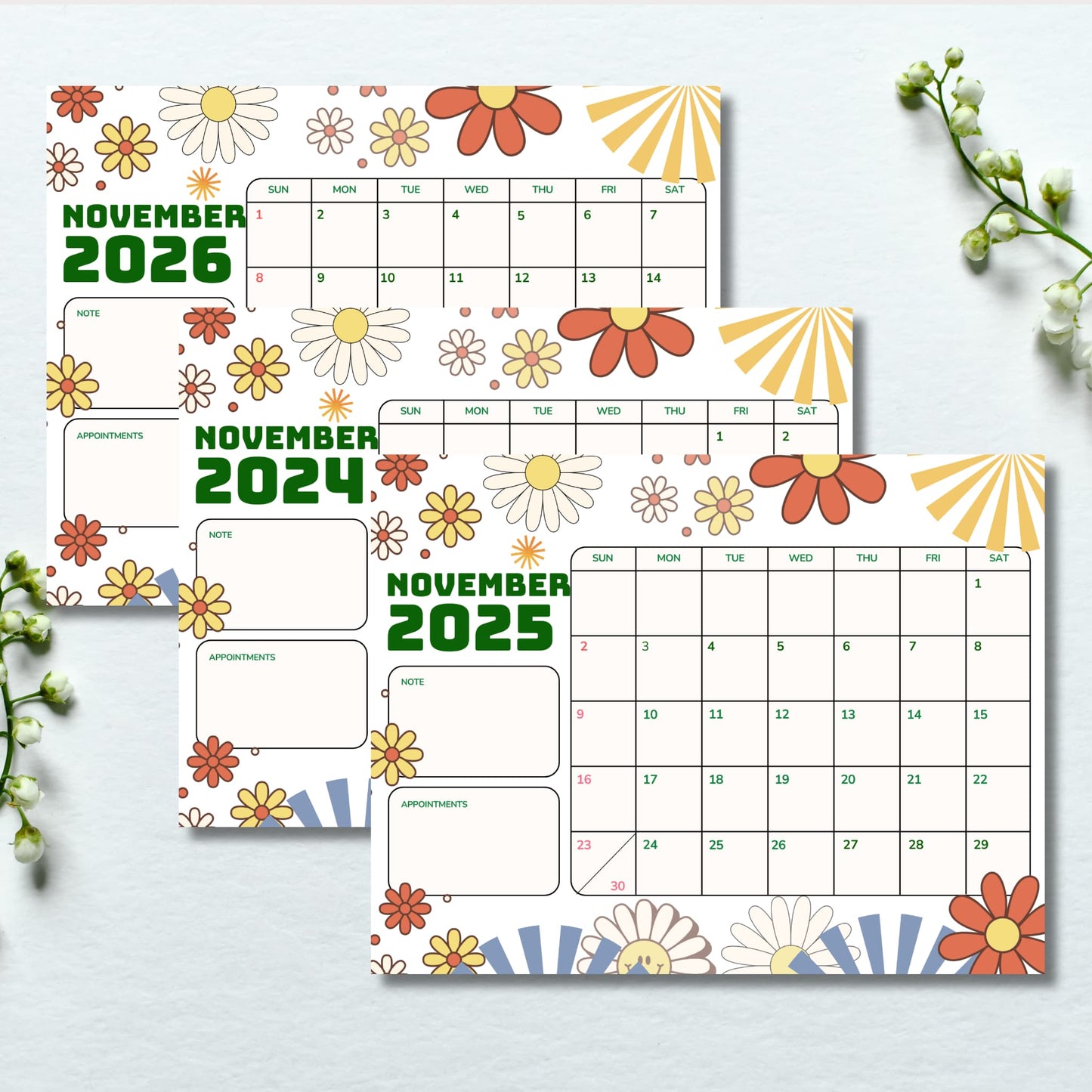 Flat lay of three November calendars 2024-2026 with orange and yellow daisy motifs, styled with white lily of the valley flowers on light background