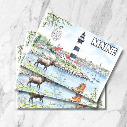 Maine striped lighthouse postcards with moose in water lily pond. Multiple prints stacked on marble background featuring pine cones and L.L.Bean boots.