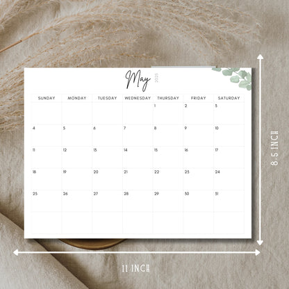 May 2025 minimalist calendar showing 11x8.5 inch dimensions, featuring clean typography, eucalyptus corner detail, displayed on natural linen backdrop