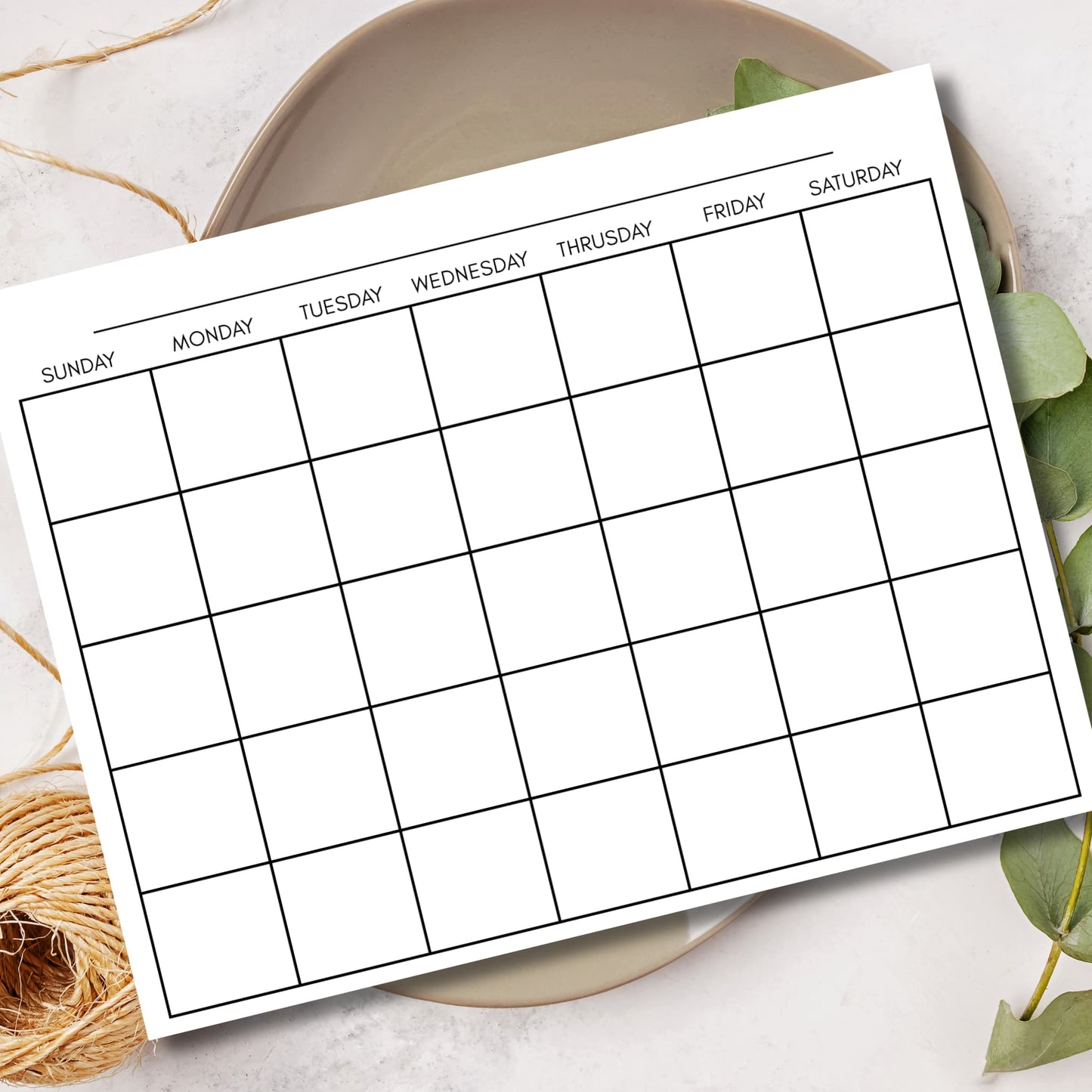 Clean monthly calendar grid displayed in ceramic bowl with eucalyptus leaves for home office decor.