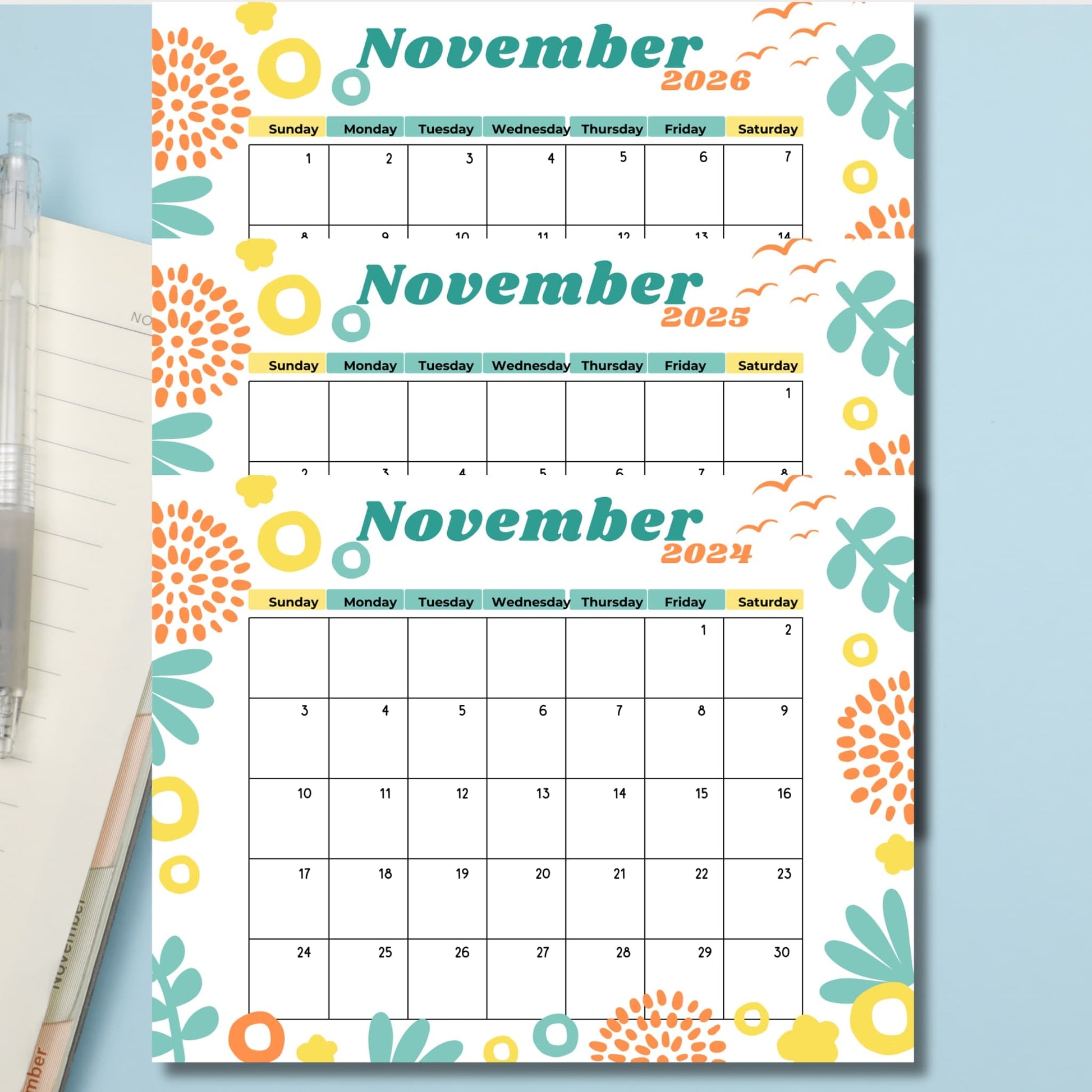 Three-year November calendar featuring mint green leaves, orange bursts, and yellow circles on white background with color-coded weekday headers in pastel shades, styled on blue surface.