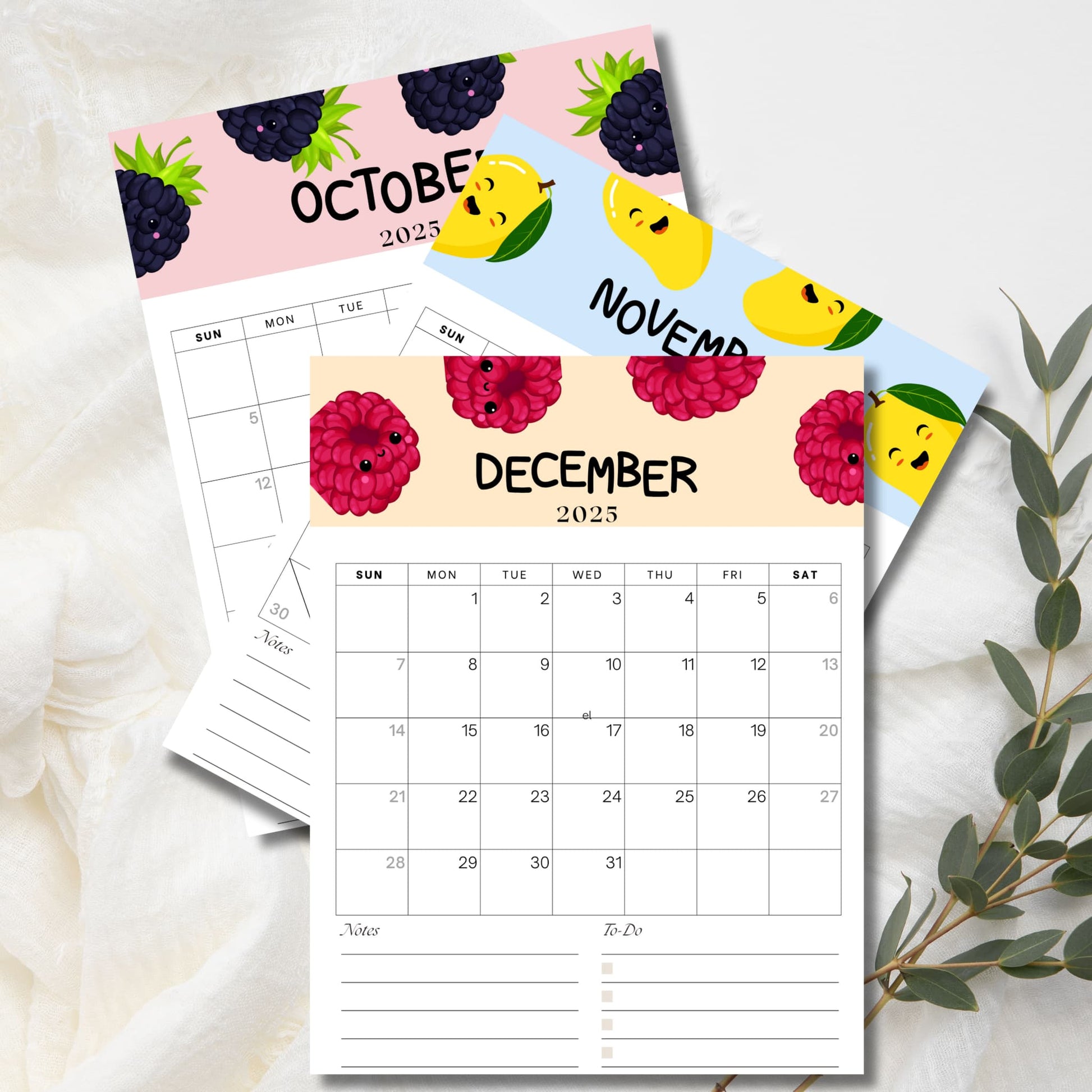 Three-month view of 2025 Kids Calendar featuring October (blackberries), November (lemons), and December (raspberries) with kawaii fruit characters. December calendar page shows complete month grid with notes section and is displayed with eucalyptus sprigs.