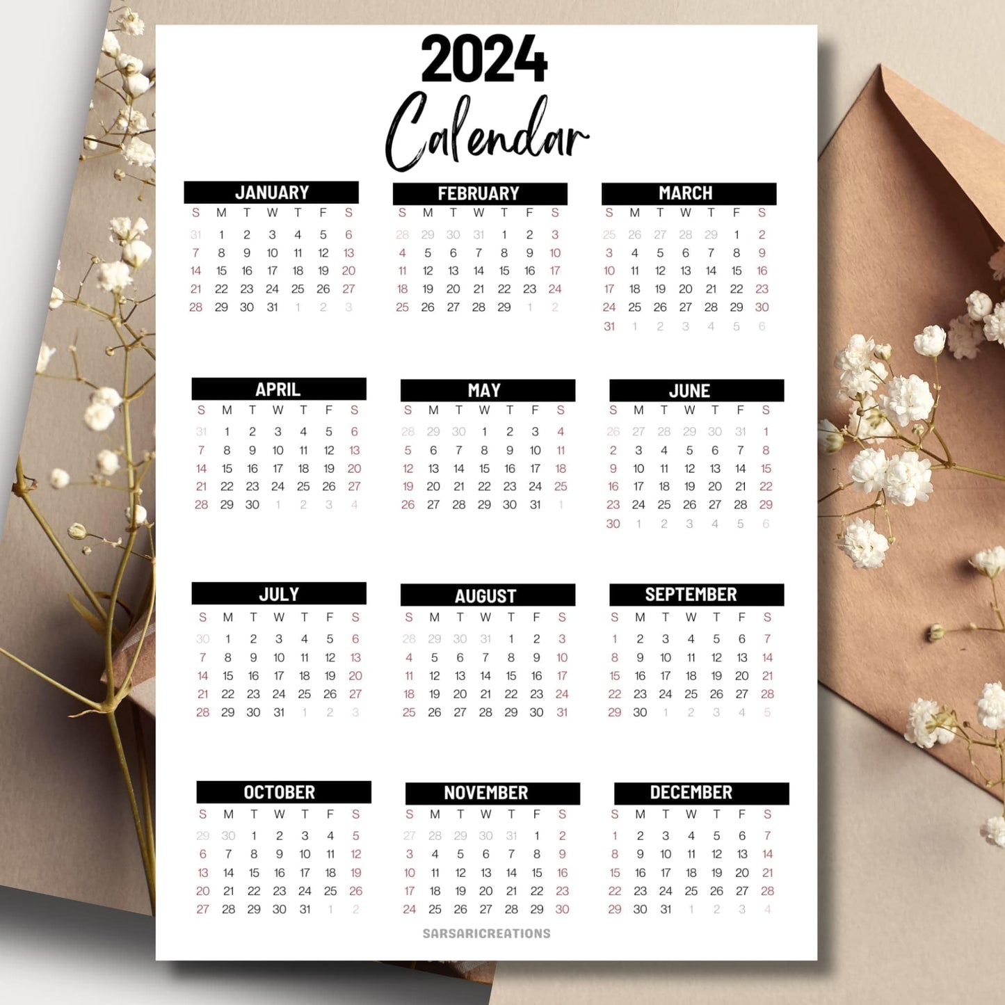 Office essential 2024 full year calendar on a table with an envelope and small white flowers in the background.