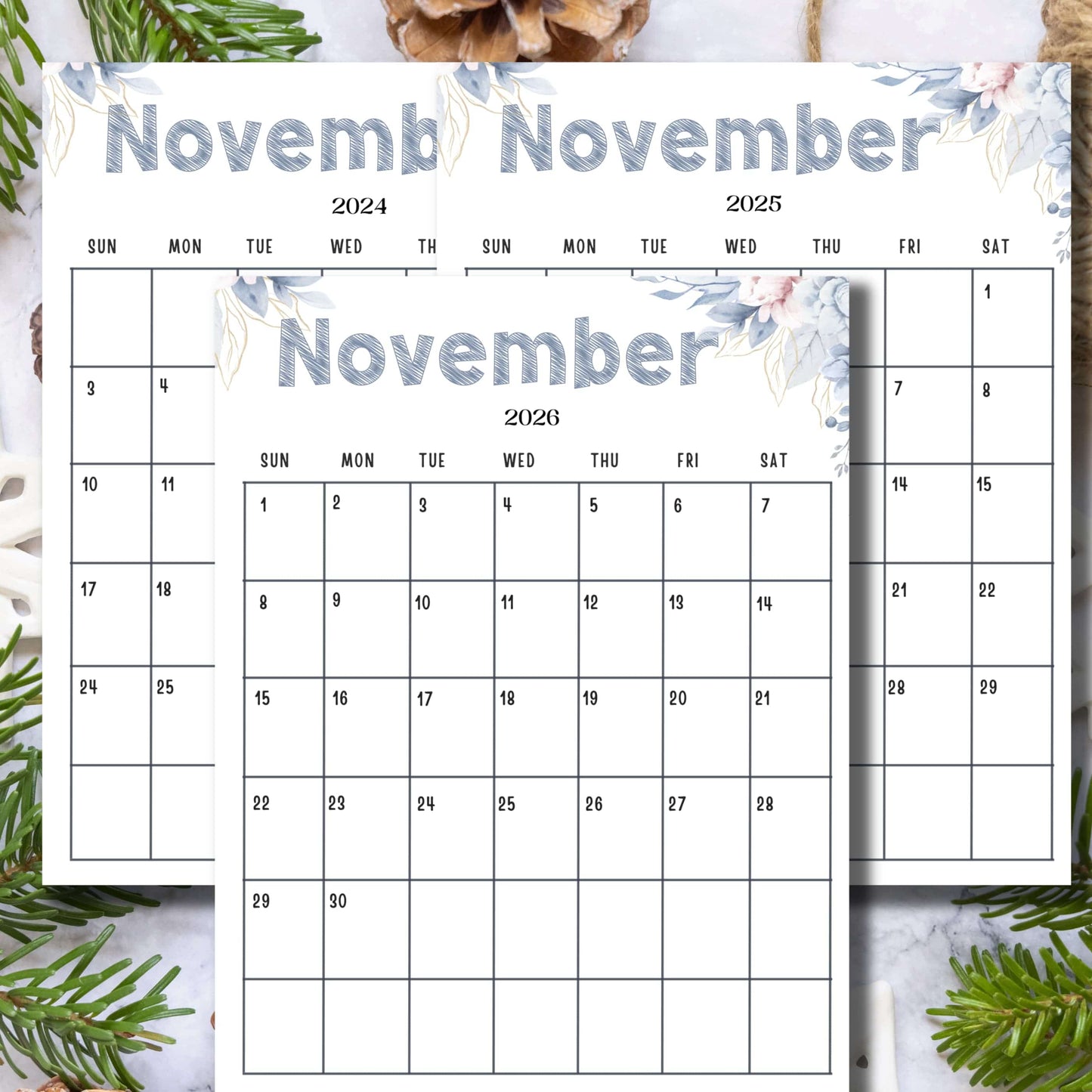 Three-year November calendar with sketched title and blue-pink watercolor florals, styled with pine branches and pinecones on marble background