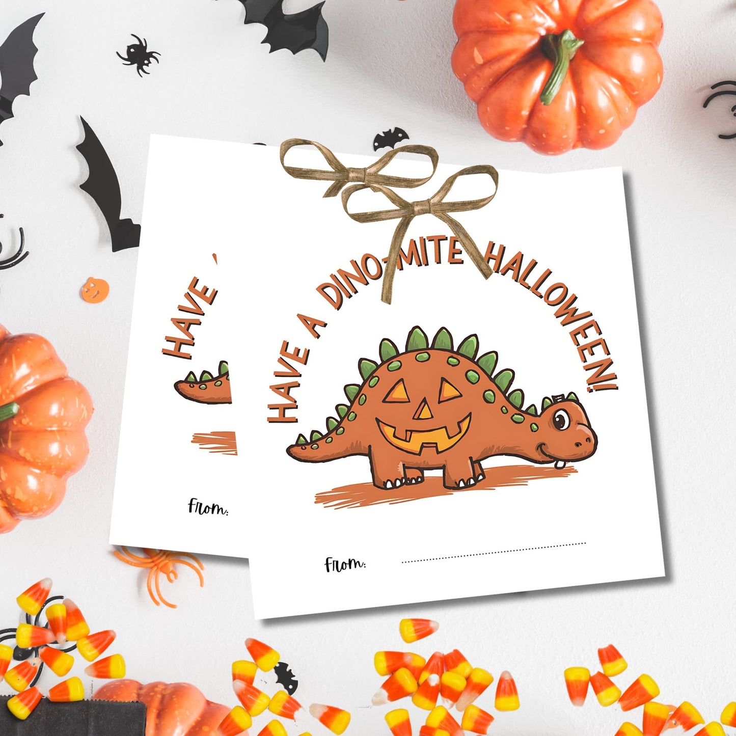 Orange dinosaur-pumpkin Halloween gift tags with "Have a Dino-mite Halloween" text, displayed with festive decorations and candy corn