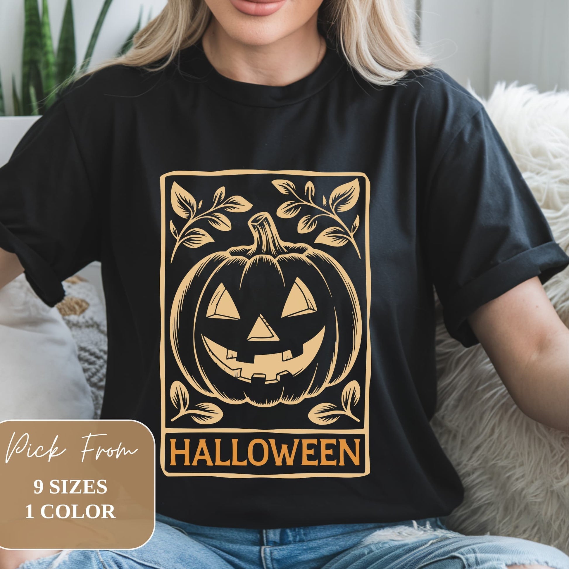 Black t-shirt with golden print featuring a stylized jack-o'-lantern in a rectangular frame, surrounded by leaf motifs. 'HALLOWEEN' text underneath. Worn by model seated on couch. Overlay indicates 9 sizes available in 1 color.