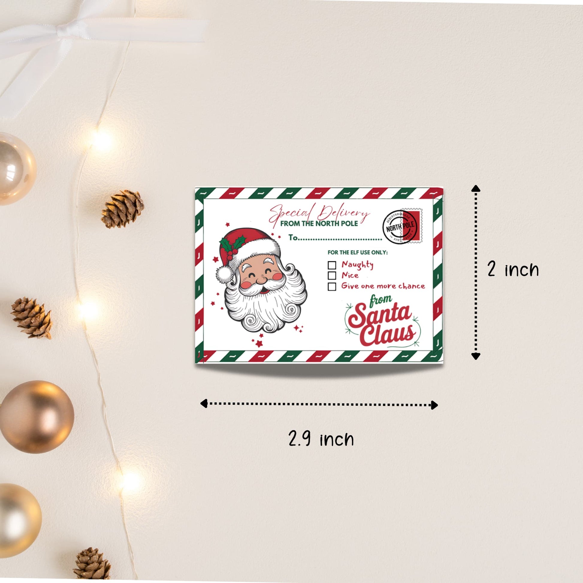 Size demonstration showing 2.9 x 2 inch dimensions of Santa Claus Special Delivery tag, with pinecones and gold ornaments for scale